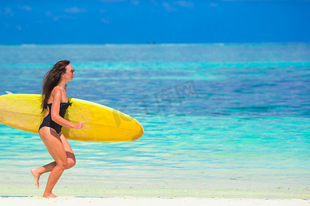 白色沙滩上带黄色冲浪板的快乐身材匀称的冲浪女人