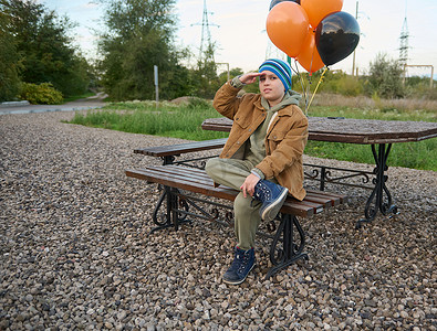 一大把气球摄影照片_英俊的少年带着黑色和橙色的气球，坐在木岸上，期待着。