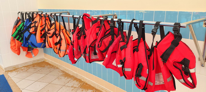 几件红色和橙色的救生衣挂在衣架上，靠近 gouboi 瓷砖墙