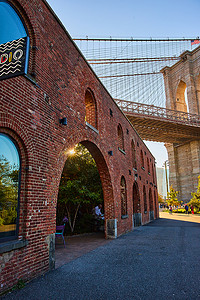 纽约市令人惊叹的标志性布鲁克林大桥旁边的砖砌建筑，拱门和金色的阳光透过