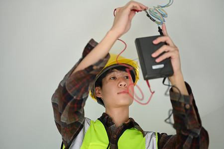 电流logo摄影照片_使用万用表测量电力线电压和电流的亚裔男性电工