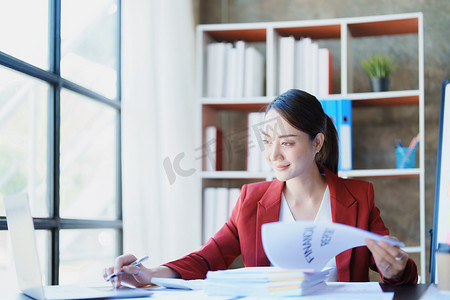 财务报表分析报告摄影照片_一位深思熟虑的亚洲女商人的肖像，她正在使用办公桌上的电脑查看财务报表并制定营销计划