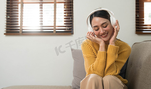 手机播放摄影照片_在家放松的微笑女孩，她正在用智能手机播放音乐，戴着白色耳机