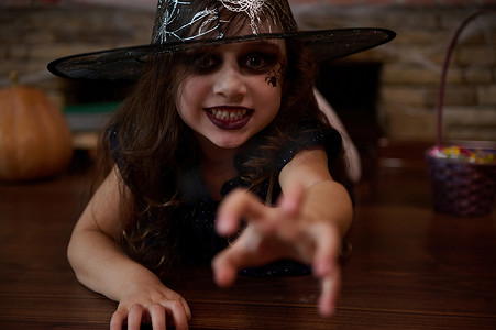 小魔女摄影照片_一个戴着魔法帽的小女巫伸出了手，一脸惊恐的看着镜头。
