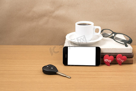 咖啡车摄影照片_办公桌：咖啡和带车钥匙的电话、眼镜、一堆