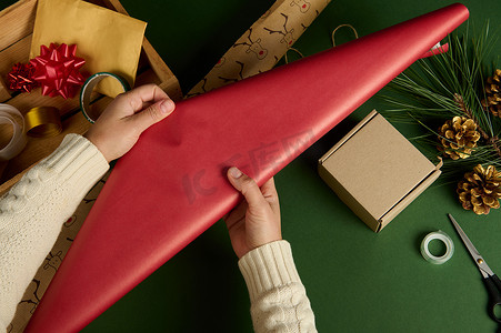 女人的手在绿色背景上铺开红色装饰包装礼品纸。