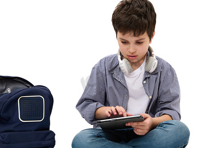 白人聪明的小学生，坐在背包旁，用数字平板电脑做学校项目的男孩