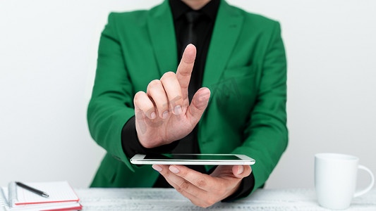 身穿绿色夹克的商人坐在桌旁，拿着手机，用一根手指指着重要信息。