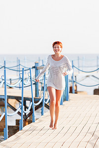 宽阔的微笑着红色短发的年轻女子在木码头上奔跑。