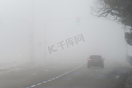 行驶着的汽车摄影照片_汽车在雾蒙蒙的路上行驶，车头灯或前灯亮着。