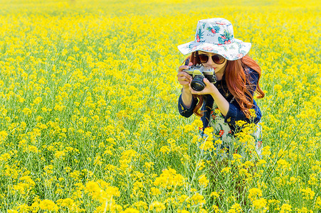 英伦花边框摄影照片_在油菜花边拍照的女人