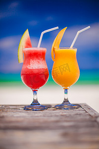 黄色西瓜摄影照片_令人惊叹的绿松石海背景中的两杯鸡尾酒新鲜西瓜和芒果