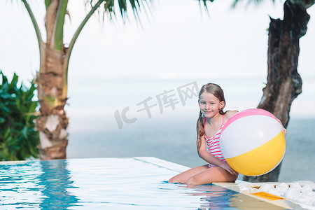 在室外游泳池玩充气玩具球的微笑可爱女孩