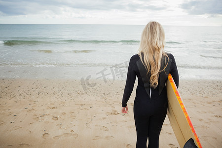 在海滩上穿着湿衣服和冲浪板的女人的后视图