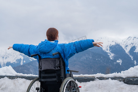 坐在轮椅上的女人的后视图在冬天的山中像翅膀一样张开双臂。
