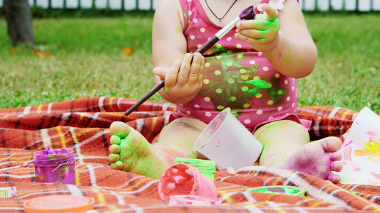 一个小孩，一个一岁大的女孩玩耍，用手指画画，装饰自己，在花园里，坐在毯子上，床罩上，在草地上，草坪上，在夏天。