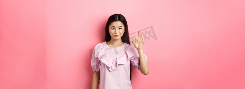 优秀青少年摄影照片_微笑的亚洲女性穿着裙子，表现出好的迹象，赞美和赞美好事，赞成优秀的选择，站在粉红色背景中