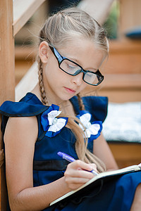 笔记背摄影照片_有室外笔记和铅笔的可爱的小女学生。