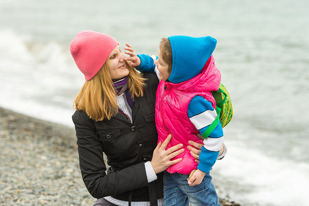 在沙滩上玩得开心的小女孩穿着暖和的衣服摸妈妈的鼻子
