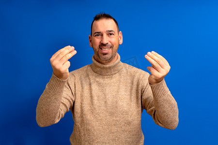 大约 40 多岁的西班牙裔男子留着胡子站在孤立的蓝色背景上，用手和手指自信地表达意大利手势。