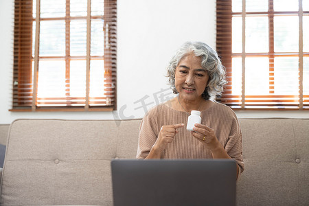 亚洲老年人在家中客厅使用笔记本电脑视频会议与医生讨论疾病和处方药 健康生活方式 居家养老概念