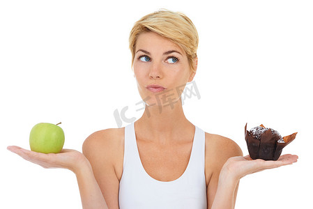 嗯嗯嗯摄影照片_嗯，也许一个松饼不会伤害……一个年轻女子一手拿着苹果，另一只手拿着甜点——孤立的形象。