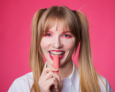 一位年轻女子的画像，她戴着牙套，妆容艳丽，口香糖在粉红色的背景上。