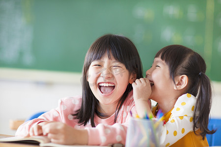 可爱小女孩摄影照片_欢笑的小女孩在课堂上分享秘密