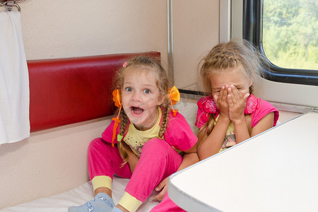 两个性格开朗的小女孩穿着同样的睡衣坐在二等车厢的火车上
