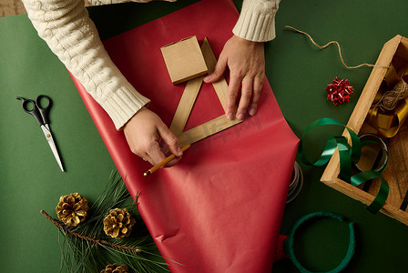 女人用尺子在礼品纸上画画，计算包装圣诞礼物所需的包装材料数量