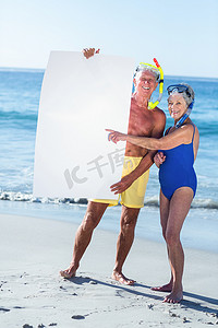 拿着一张白色海报的海滩设备的资深夫妇