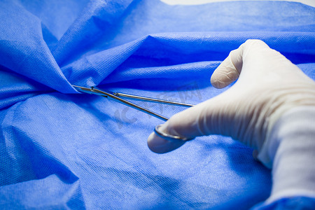 医生手中的手术钳，在蓝色背景下，工作室拍摄。