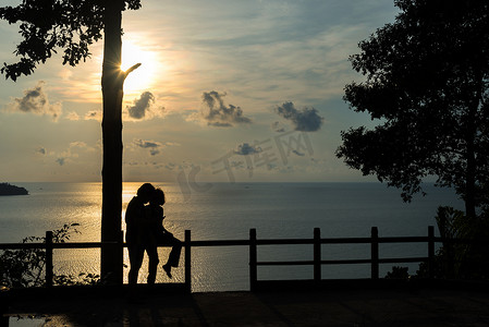 日落时在海滩上拥抱和看太阳的情侣剪影