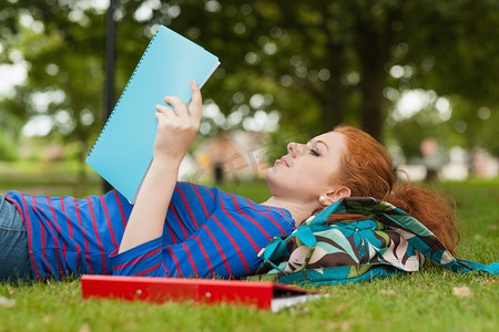 华丽的严肃学生躺在草地上阅读笔记