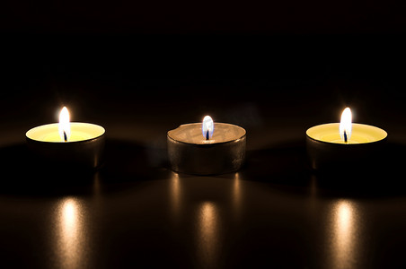 三根蜡烛摄影照片_三根燃烧的蜡烛在黑暗中