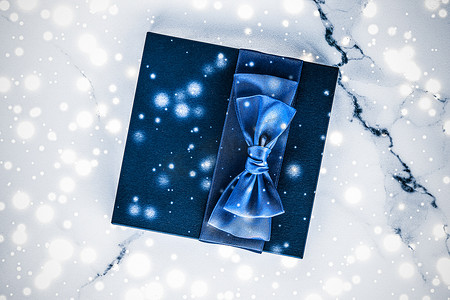 蓝色品牌展示摄影照片_有蓝色丝绸弓的寒假礼物盒，大理石上的雪闪闪发光