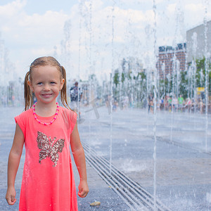 阳光明媚的炎热日子里，小可爱女孩的画像在街头喷泉里玩得开心