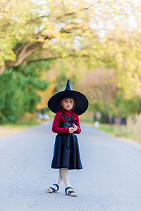 在万圣节派对上，穿着女巫服装的小女孩站在路上