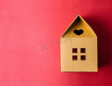城市建筑模型摄影照片_红色背景上的棕色纸房子折纸，带有空白空间供您的文字或消息使用。