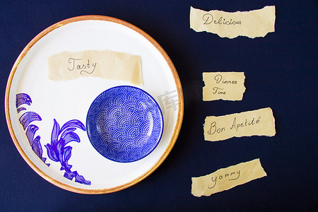 美味，美味，晚餐时间的字母和文字，空的蓝色餐具，蓝色桌子上的碗和盘子。