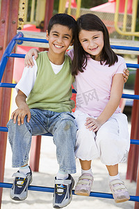 坐在游乐场结构上微笑的两个幼儿