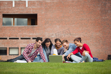 五名随便的学生坐在草地上指着笔记本电脑