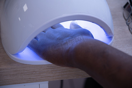 客户的手放在紫外线灯中，用于固定凝胶抛光、特写、柔焦