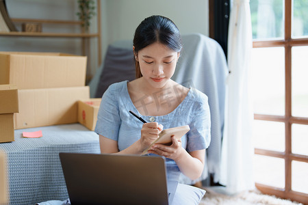 独立产品摄影照片_独立的年轻亚洲女性在线卖家的小企业主正在使用计算机并接受订单来包装产品以交付给客户。