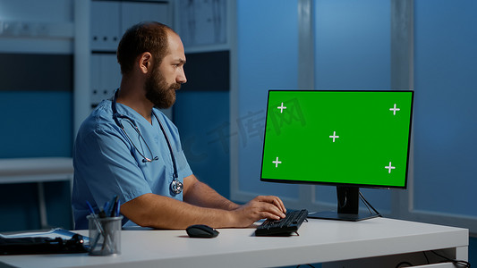 坐在办公桌前的执业男护士在带绿屏的电脑上输入病人疾病报告
