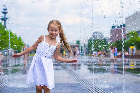 阳光明媚的炎热日子里，快乐的小女孩在街头喷泉里玩得开心