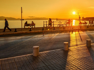 江边日落摄影照片_塞萨洛尼基，希腊 在江边的黄金时段与路过的人群。