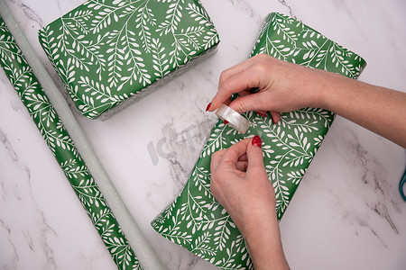 女人手上涂着红色圣诞美甲，用绿色包装纸包裹礼物