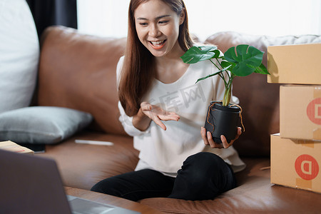 在做出购买决定之前，使用电脑向客户展示产品的独立年轻亚洲女性在线卖家的小型企业创业者。