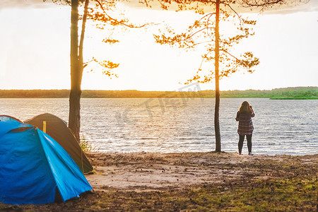野营摄影照片_湖后女孩的轮廓，森林中的营地，帐篷里的旅行和度假，野营的户外生活方式